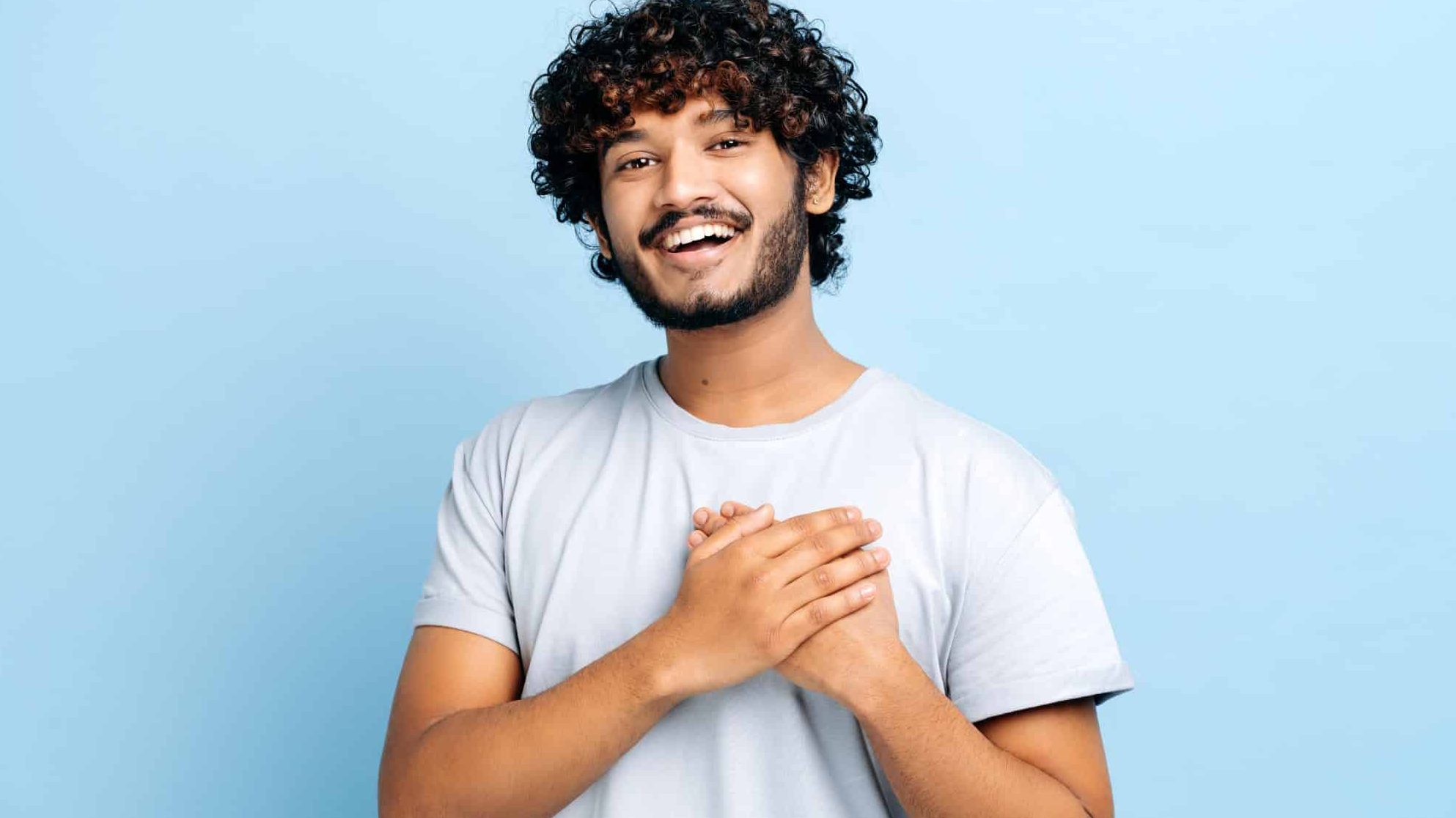 Un homme en t-shirt bleu sourit et a les deux mains sur le coeur