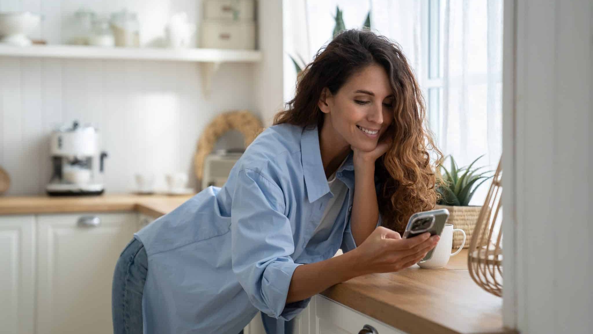 Une femme sourit en regardant son téléphone.