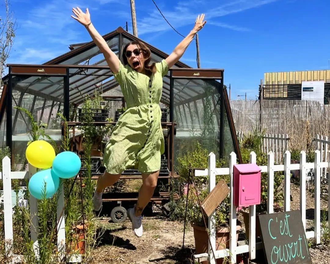 Ophélie Damblé saute de joie devant l'une des serres de sa pépinière installée à Pantin sous un beau ciel bleu azur.