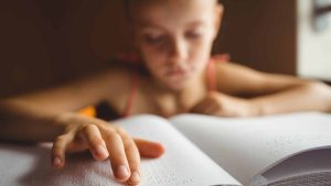 Une enfant malvoyante lit un ouvrage en braille.