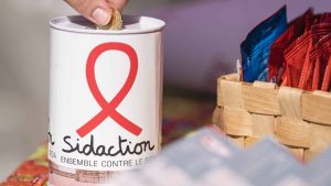 Une personne fait un don d'une pièce dans une tirelire Sidaction