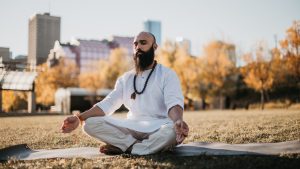 Un homme est assis par terre sur un tapis de yoga. Il a les yeux fermés.