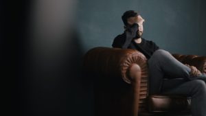 Un homme est assis sur un canapé la il se couvre les yeux avec sa main droite